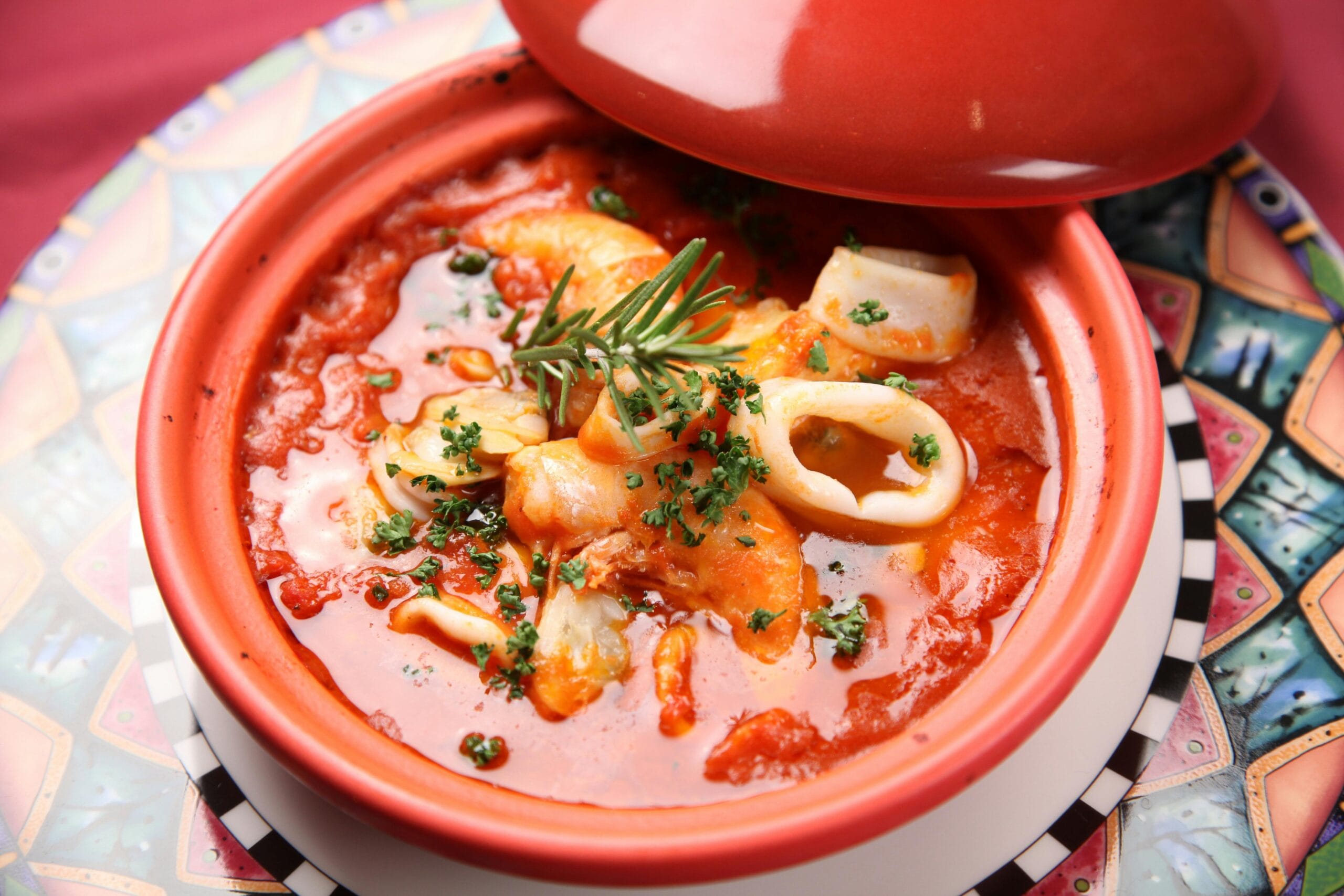 A vibrant and tasty homemade squid and tomato stew garnished with fresh herbs in a ceramic pot.