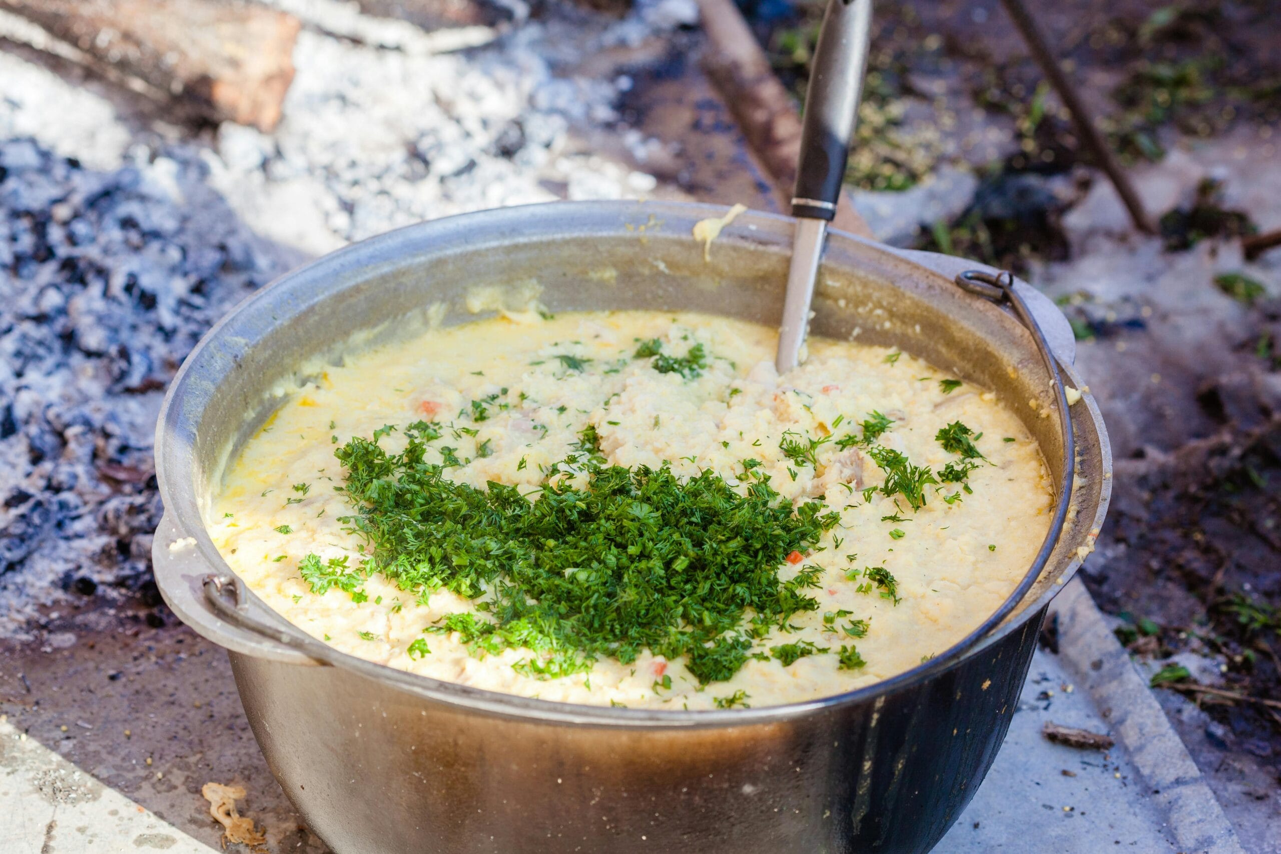 A large pot of delicious soup cooked outdoors with fresh parsley as garnish. Perfect for campfire cooking.